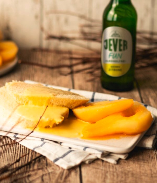 Ein Teller mit Käse, Obststücken und Brot neben einer Flasche auf einem Holztisch.
