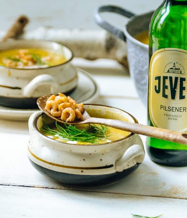 Zwei Keramiktassen mit Suppe stehen auf einem Holztisch, Löffel liegen obenauf.