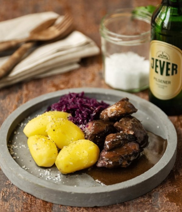 Ein Teller mit Kartoffeln, geschmortem Fleisch und Rotkohl steht neben Besteck und Salz.