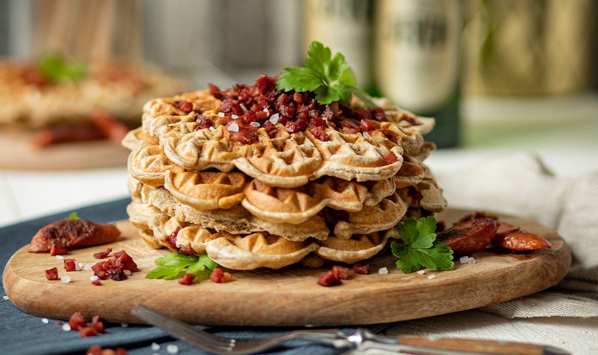 Ein Stapel Waffeln ist mit Kräutern und Würfeln aus gebratenem Speck belegt.