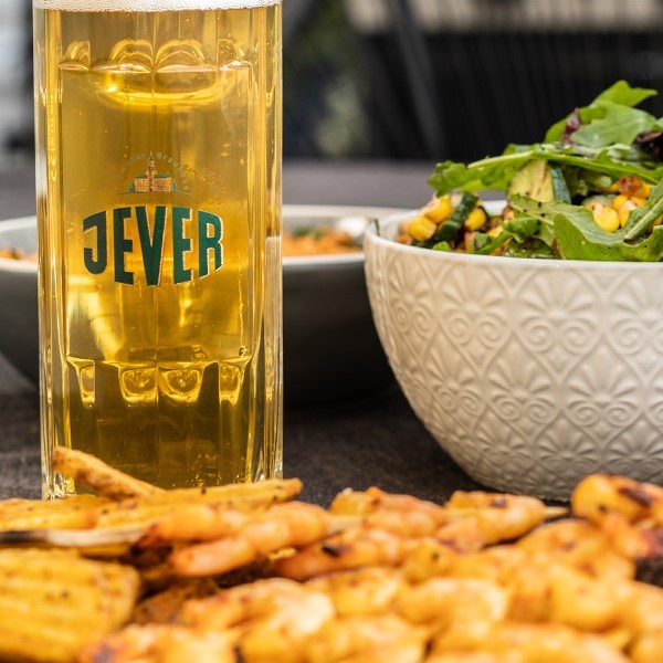 Ein Glas Bier steht vor einer Schüssel Salat und gegrillten Garnelen.