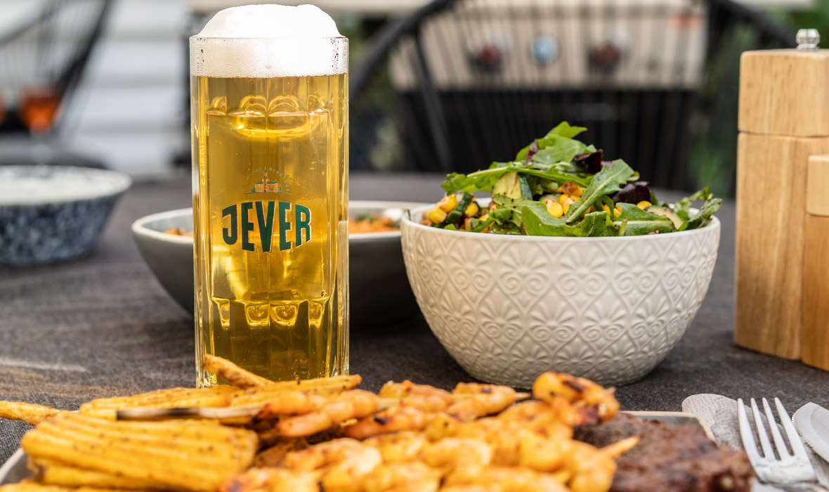 Ein Bierglas steht neben Grillgerichten und einem Salat auf einem Tisch.