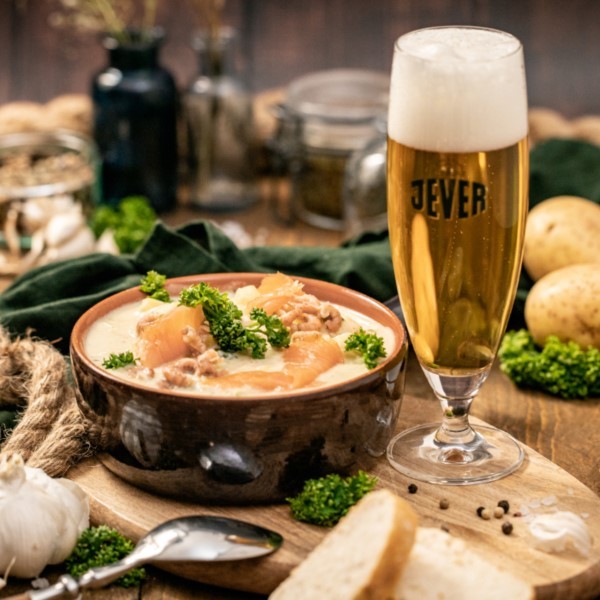 Ein Teller mit Eintopf und gehackter Petersilie sowie ein Glas helles Bier stehen auf einem Holztisch.