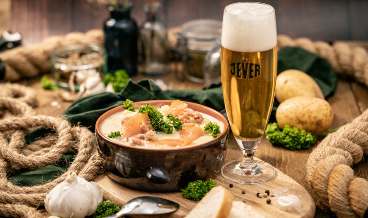 Eine Schüssel mit Eintopf und glas gefüllt mit Bier stehen auf einem Holztisch.