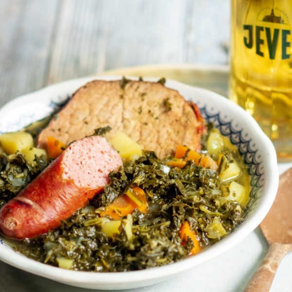 Ein Teller mit Grünkohl, Kartoffeln, Wurst und Kassler, neben einem Glas Bier.