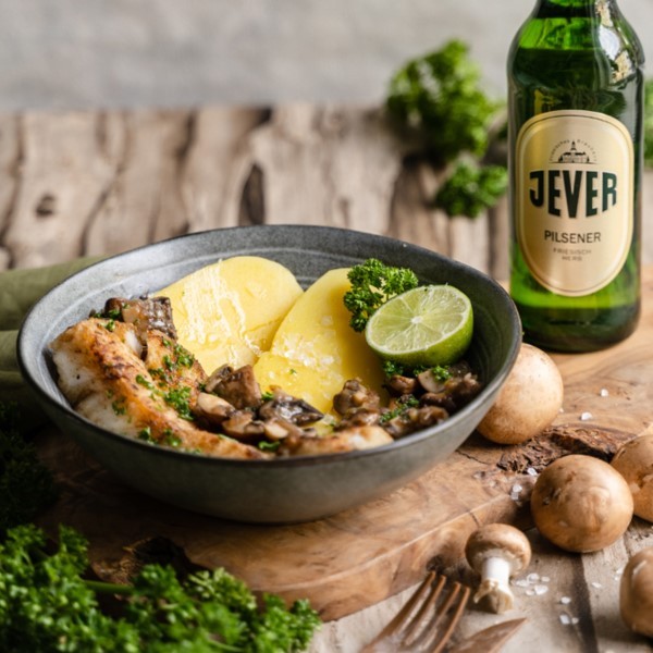 Gebratenes Hühnchen mit Kartoffeln und Pilzen wird in einem Teller serviert. Nebenan steht eine Flasche Bier.