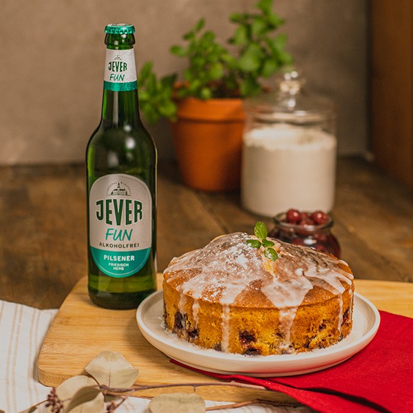 Eine Fruchttorte mit Glasur steht auf einem Tisch neben einer Flasche Bier.