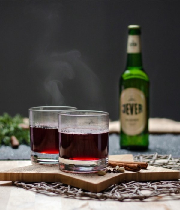 Zwei Gläser mit dunkler Flüssigkeit stehen auf einem Holzbrett, dahinter eine Flasche.