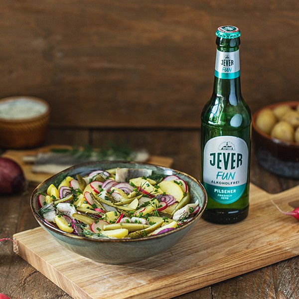 Eine Flasche alkoholfreies Bier steht neben einer Schüssel mit buntem Salat auf einem Holztisch.