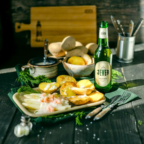 Ein Teller mit gebratenen Kartoffeln und Spargel steht neben einer Flasche Bier.