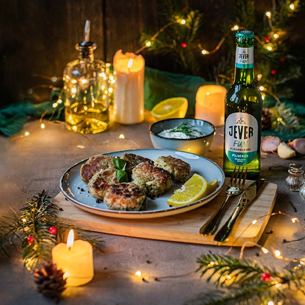 Ein Teller mit Frikadellen liegt auf einem Holztisch, umgeben von Kerzen und einer Bierflasche.