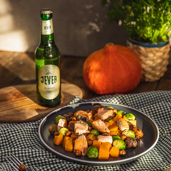 Ein herbstliches Gericht mit Lachs, Kürbis und Rosenkohl liegt auf einem Teller neben einem Bier.