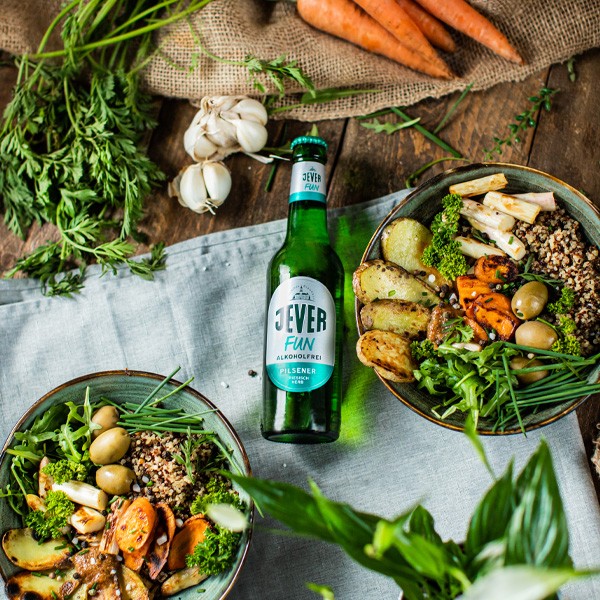 Eine Flasche alkoholfreies Bier steht neben zwei Schüsseln mit frischen Gemüsegerichten.