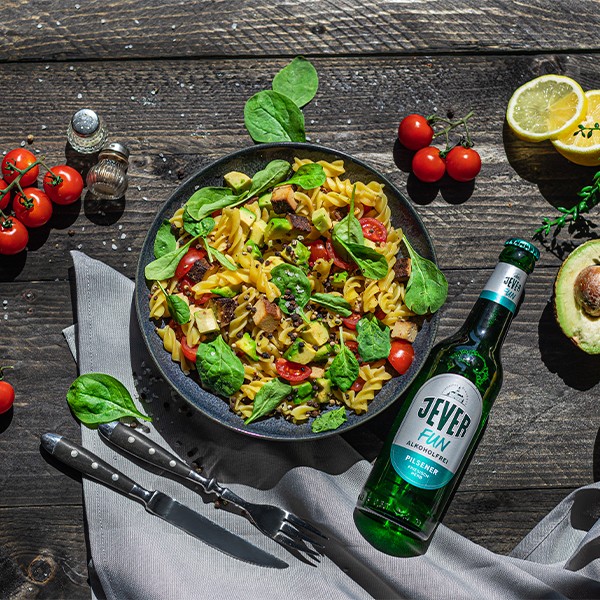 Ein Teller mit Nudelsalat, Gemüse und Blattspinat liegt neben einer Flasche Wasser.
