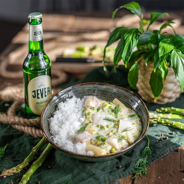 Ein grüner Teller mit Fischcurry und Reis neben einer Flasche Bier steht auf einem Holztisch.
