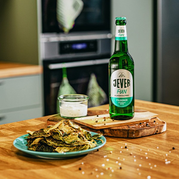 Eine Flasche alkoholfreies Bier steht neben einem Teller mit gebratenem Spargel auf einem Holzbrett.