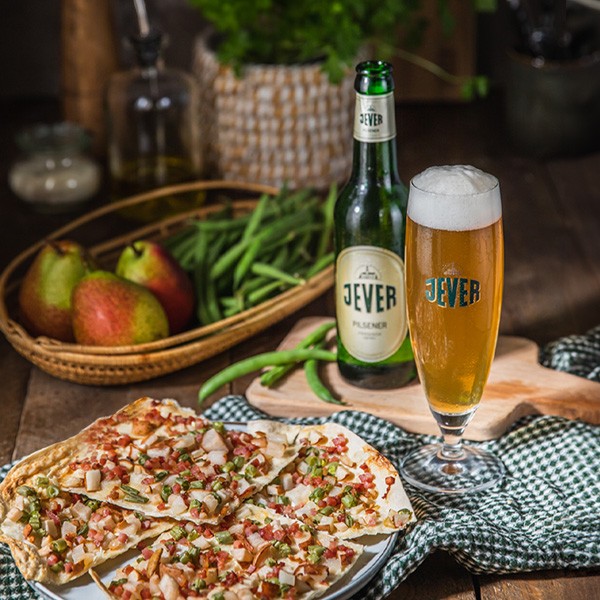 Ein Glas Bier steht neben einer Flasche und einer Pizza auf einem Holztisch.