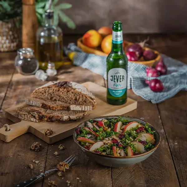 Ein appetitliches Essen auf einem rustikalen Holztisch inklusive Salat, Brot und einer Flasche Getränk.