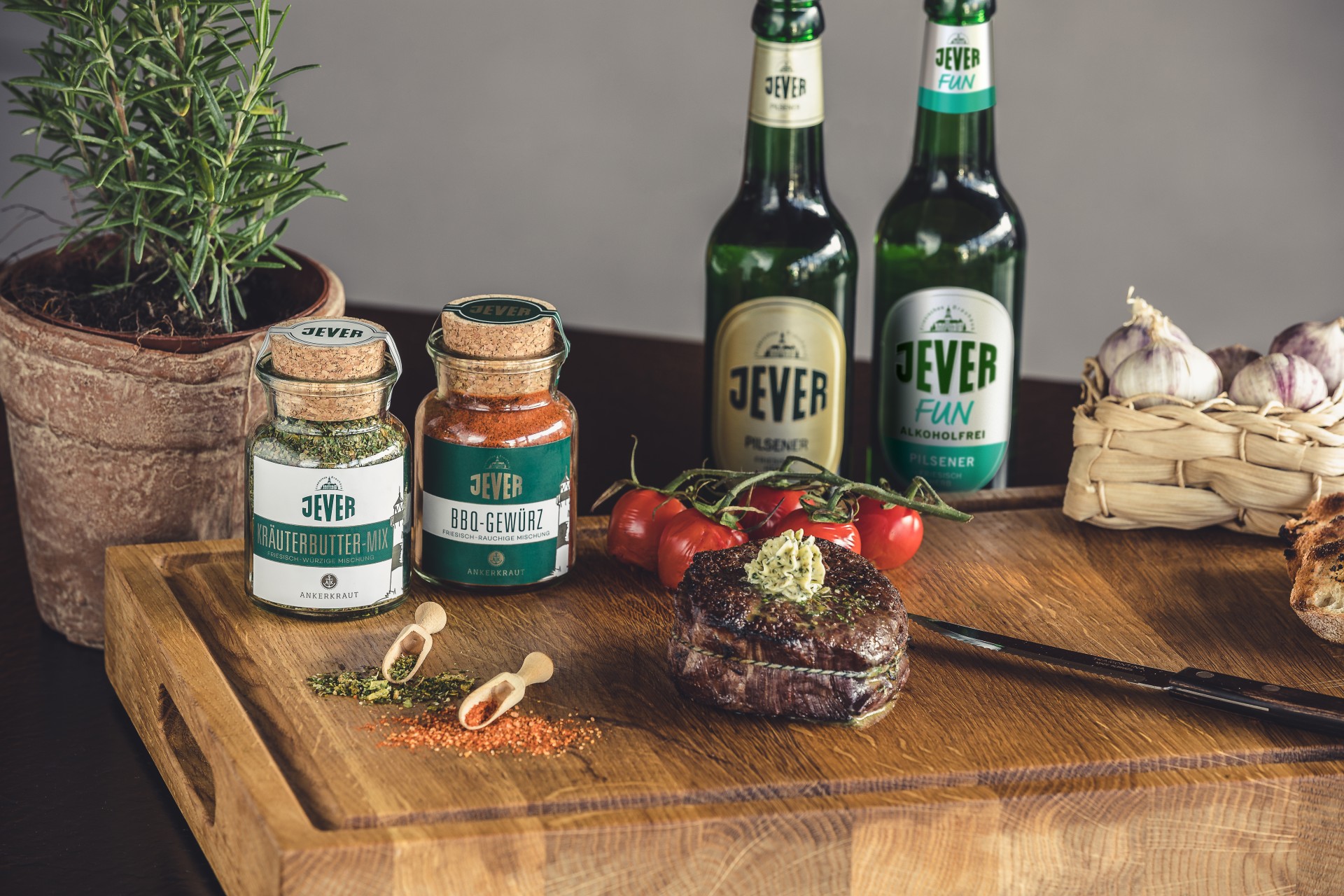 Gebratenes Steak mit Kräuterbutter auf einem Holzbrett neben Gewürzen und Bierflaschen.