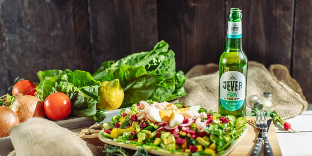 Salat mit Ei, Krabben und Gemüse neben einer Flasche Bier der Marke Jever Fun Alkoholfrei auf einem Holztisch.