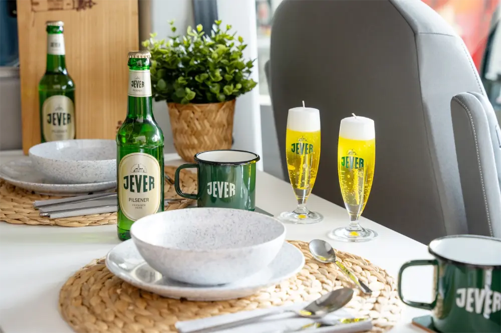 Gedeckter Tisch mit Jever Flaschen und Jever Tassen. Zwei Kerzen in Jever-Biergläser-Optik mit gelbem Wachs stehen daneben. 