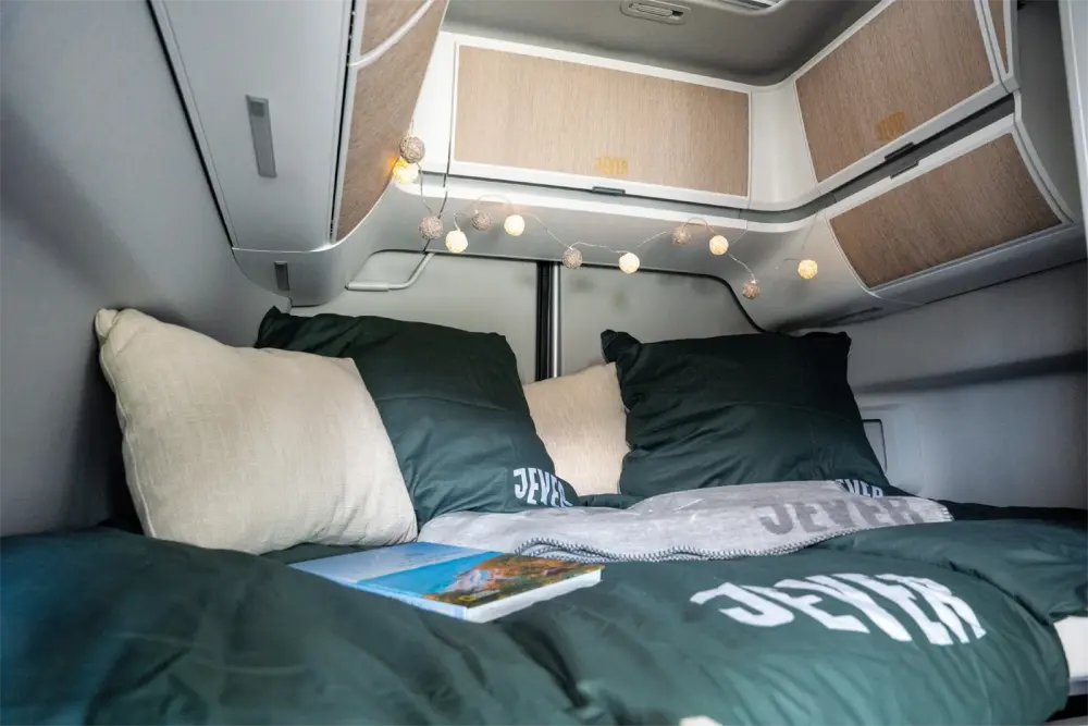 Gemachtes Bett mit Jever-Bettwäsche in Schlafkabine eines Campingvans. Oberschränke und Lichterkette im Hintergrund.