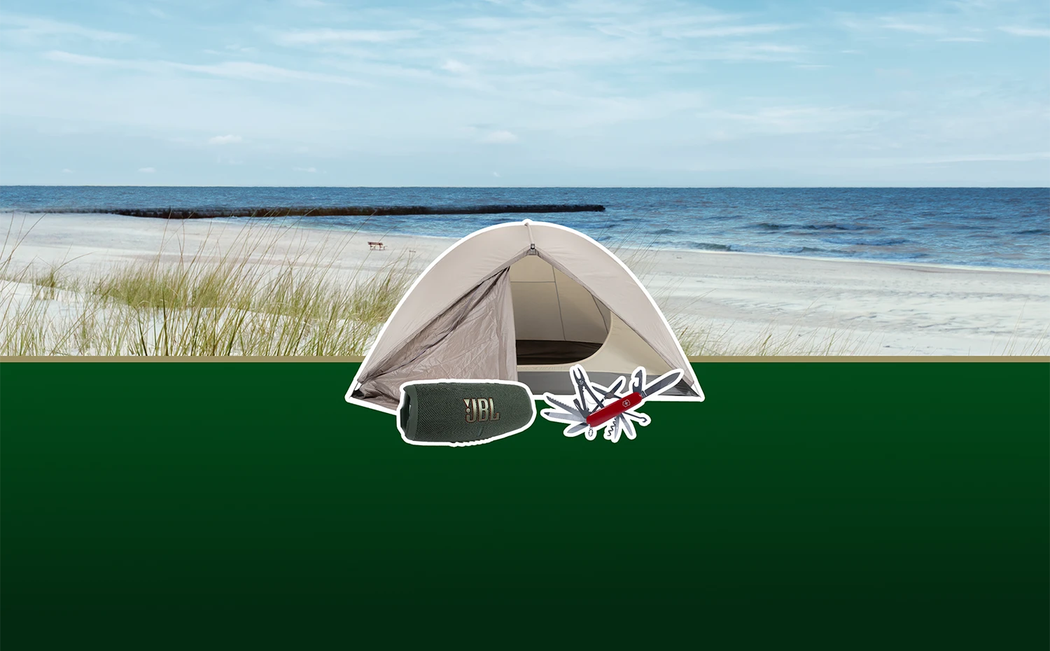 Auf grünem Boden vor Dünen und Meer steht ein geöffnetes Zelt neben einem tragbaren JBL Lautsprecher und einem Taschenmesser.