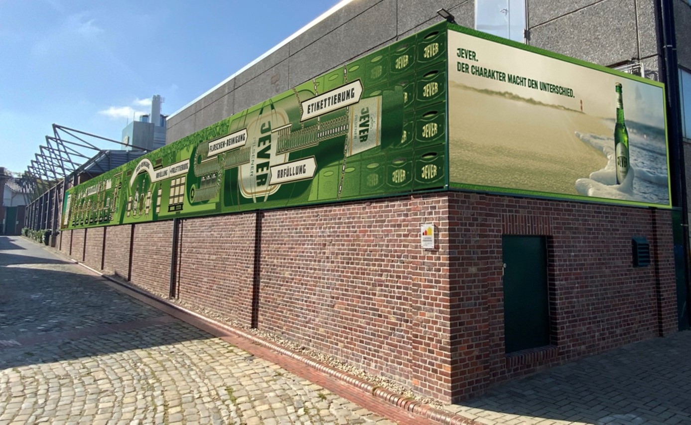Eine Backsteinmauer in einer Fabrikeinstellung ist mit einem langen Werbebanner bedeckt.