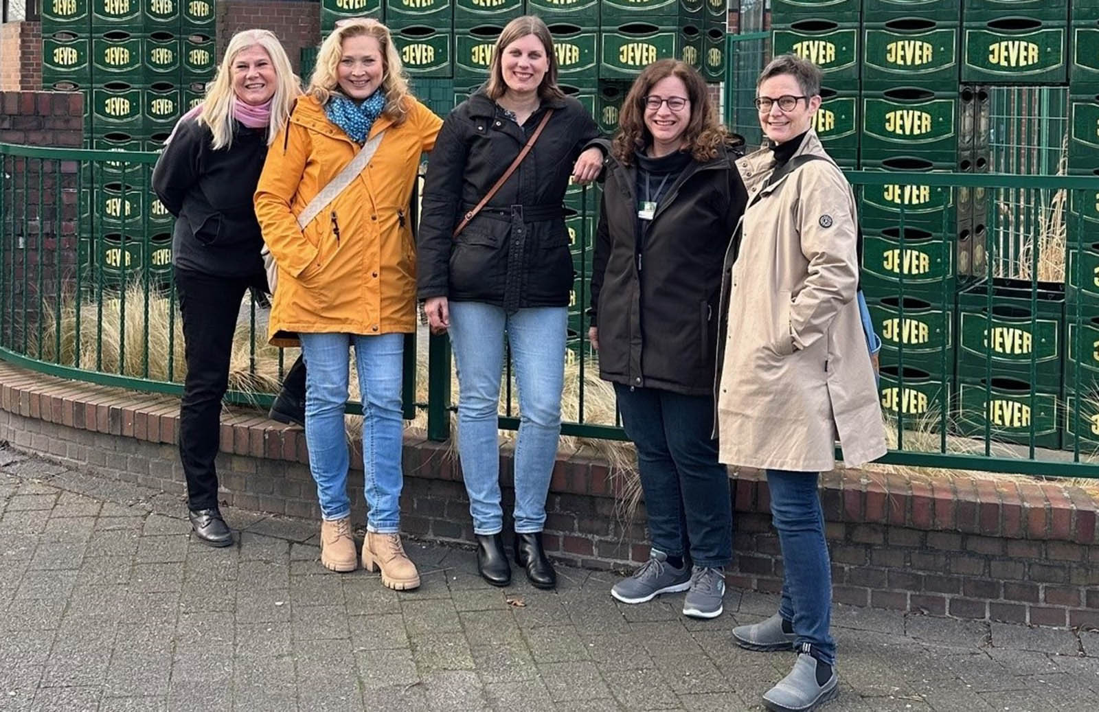 Fünf Frauen stehen lächelnd vor einer Wand aus grünen Bierkisten.
