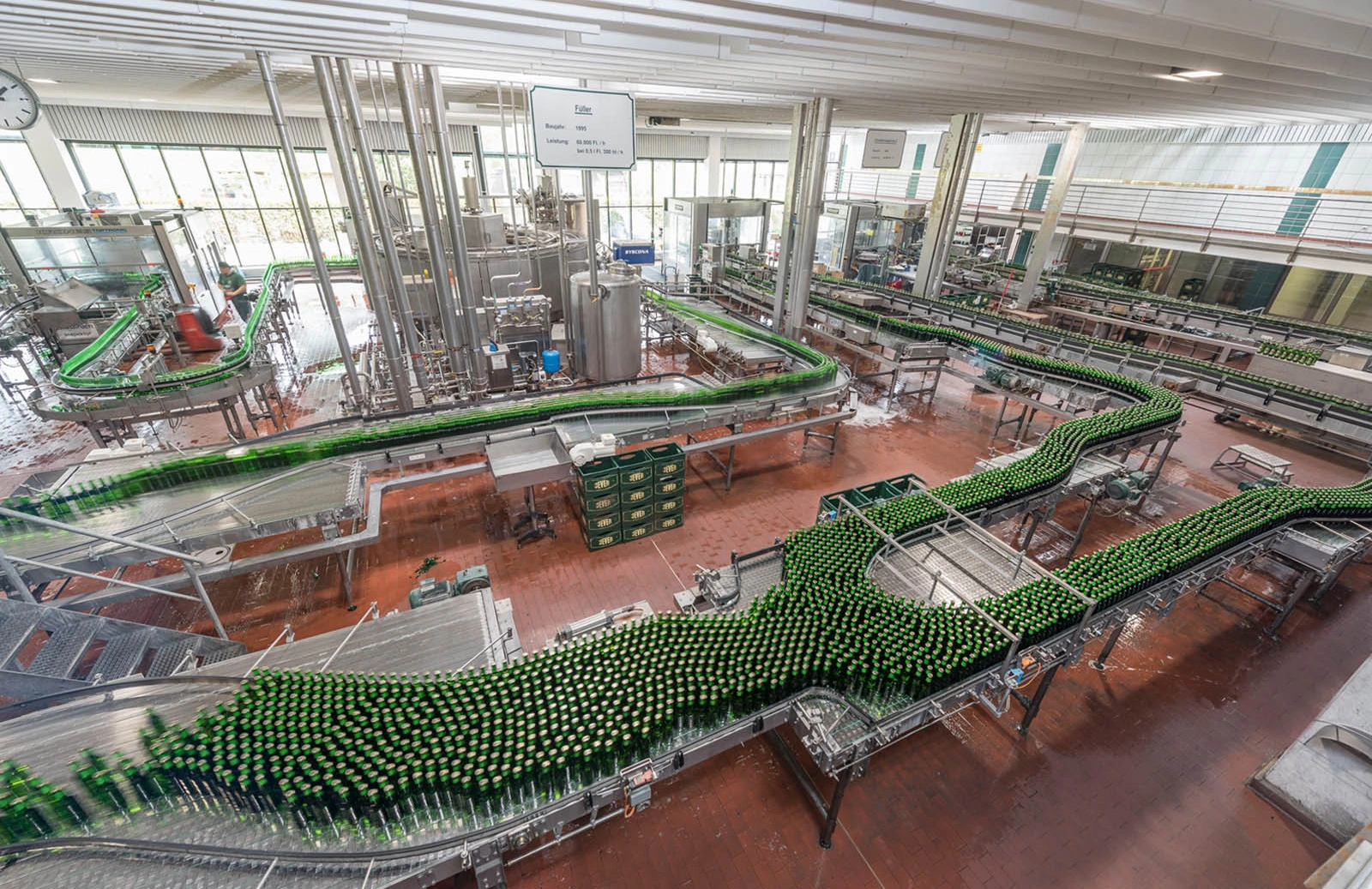 Große Flaschenabfüllanlage mit vielen grünen Flaschen auf Förderbändern in einer modernen Fabrikhalle.