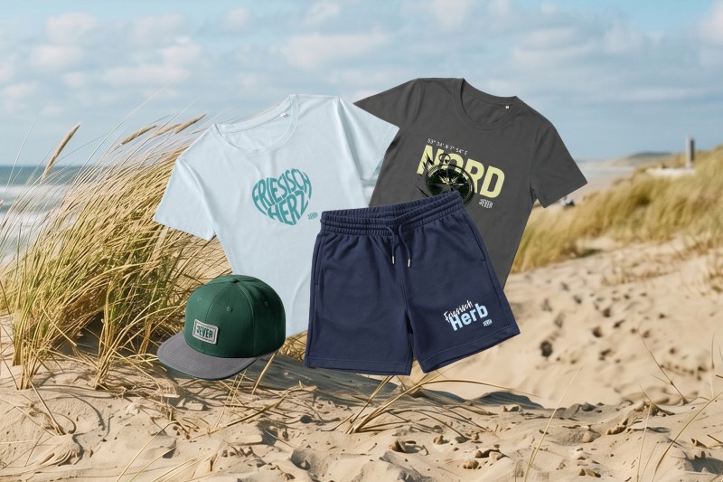Verschiedene Jever Werbemittel liegen auf einem Strandgras bedeckten Sanddüne, dahinter das Meer.